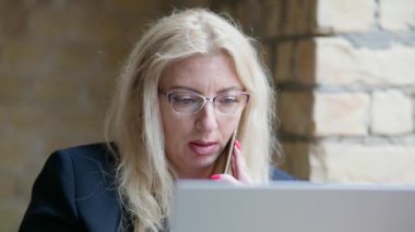 Konsantre bir kadın bir kafede tek başına oturuyor, bir dizüstü bilgisayarla çalışıyor ve telefonla konuşuyor..