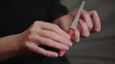 Bir kadın tırnak törpüsüyle tırnaklarını düzleştiriyor. Kadın tırnakları ve tırnak törpüsü. Çivinin kenarı hizalanmış. Evde kendine manikür yaptır..