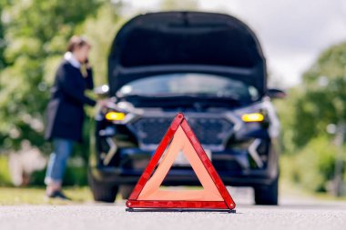 Red emergency stop sign and woman talking on the phone near a broken car on the road