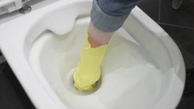 close-up of a gloved hand using a washcloth while cleaning the toilet bowl in the bathroom