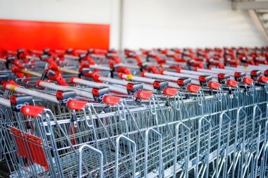 Bir süpermarketin yanında kırmızı saplı metal alışveriş arabaları var.