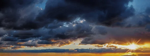 Evening golden sky over the sea at sunset. The sunset panorama is decorated with clouds of various shapes.