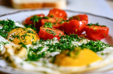 Mutfak masasında beyaz bir tabakta domatesli yumurta ve otlar..