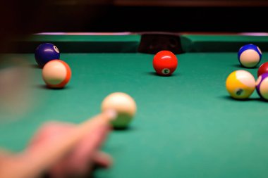 Yeşil bilardo masasında bilardo topları. Masadaki bilardo topunu işaret eden bulanık bir el.