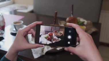 Yemek fotoğraflayan bir kadın. Bir restoranda veya kafede masada otururken akıllı telefondan hamburgerin fotoğrafını çeken bir kız. Birinci şahıs görüşü. Eller yukarı.