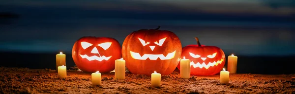 Panorama of Scary pumpkin lanterns with an evil Halloween grin. with lit candles in the sand on the seashore.