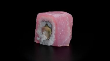 Siyah arka planda salatalık, avokado, masago ve krem peynirli ton balığı rulosu.