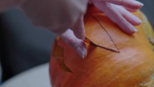 ハロウィーンパーティーのために大きなオレンジのカボチャを彫る女性 休日の気分を設定するにはナイフでカボチャのランタンに恐ろしい顔を彫る — ストック動画