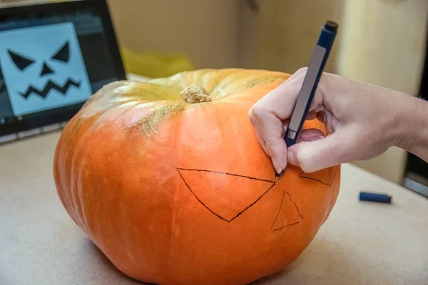 Female hands draw on a pumpkin to carve Jack-O-Lantern for Halloween party. Woman using picture on tablet as a model