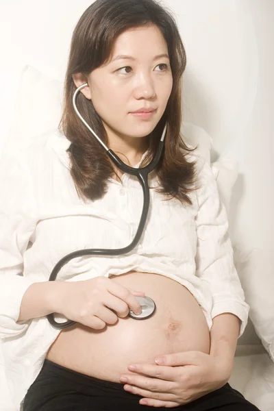 Asiática mulher grávida ouvindo seu bebê através do estetoscópio — Fotografia de Stock