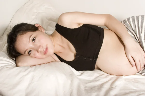 Muito bela jovem mulher grávida deitada em uma cama — Fotografia de Stock