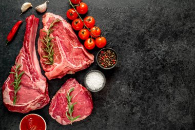 Baharatlı çiğ biftek ve siyah arka planda otlar.