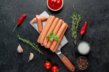 Baharatlı çiğ sosisler ve siyah arka planda bitkiler. Üst Manzara. Metnin için boş yer.