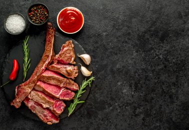 Baharatlı çiğ biftek ve siyah arka planda otlar.