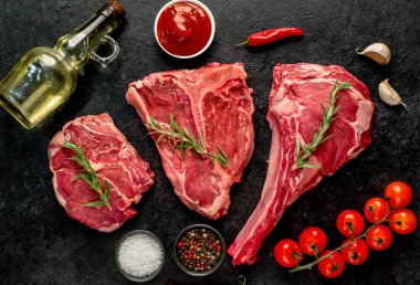 Baharatlı çiğ biftek ve siyah arka planda otlar.