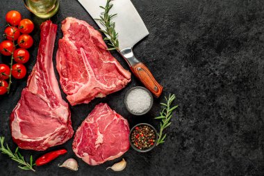 Baharatlı çiğ biftek ve siyah arka planda otlar.