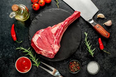 Baharatlı çiğ biftek ve siyah arka planda otlar.