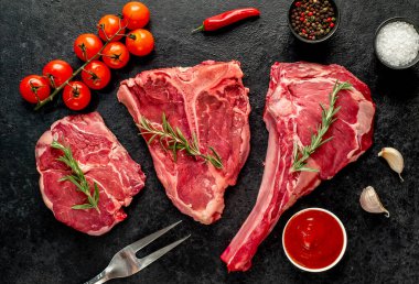 Baharatlı çiğ biftek ve siyah arka planda otlar.