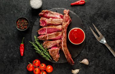 Baharatlı ızgara biftek ve siyah arka planda otlar.