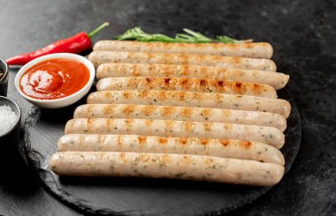 Domates soslu ızgara sosis ve siyah arka planda sebze.