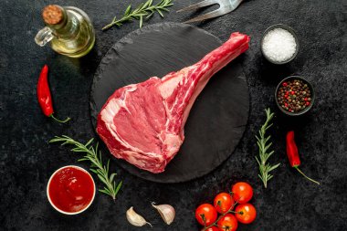 Biberiyeli çiğ biftek ve siyah arka planda baharatlar.