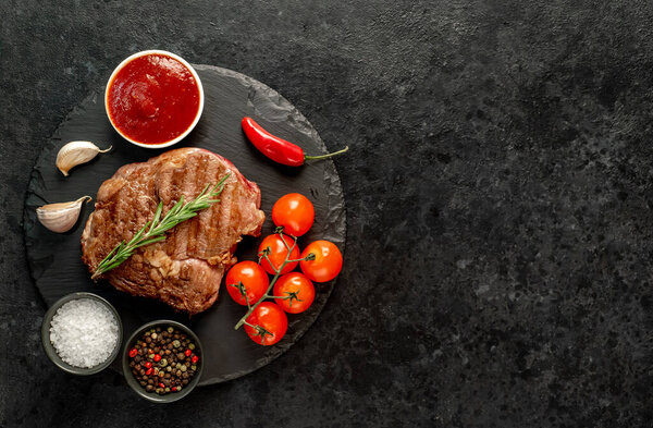 grilled beef steak with vegetables and spices on black stone background. top view. copy space.
