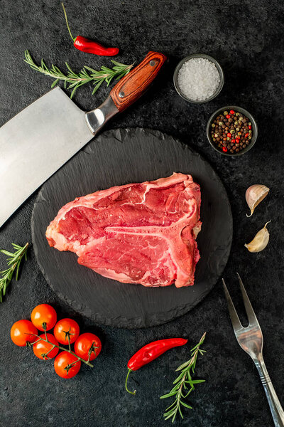 raw beef steak with spices and rosemary on black background