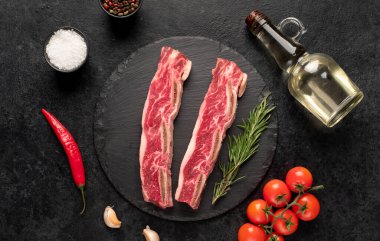 Çiğ domuz pirzolası, baharat ve siyah arka planda bitkiler.