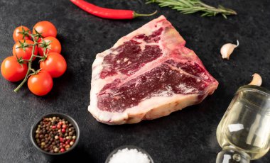 Baharatlı çiğ biftek ve siyah arka planda otlar.