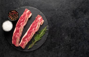 Çiğ domuz pirzolası, baharat ve siyah arka planda bitkiler.