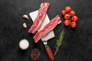 Çiğ domuz pirzolası, baharat ve siyah arka planda bitkiler.