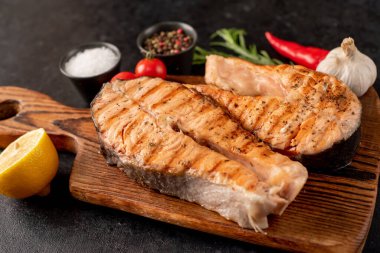 Sebzeli ızgara somon bifteği ve siyah taş arka planda baharatlar.