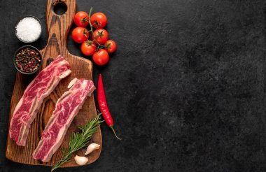 Çiğ domuz pirzolası, baharat ve siyah arka planda bitkiler.