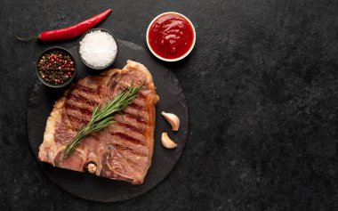 Biberiyeli ızgara biftek ve siyah arka planda baharatlar.