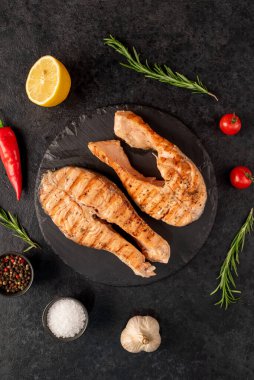 Sebzeli ızgara somon bifteği ve siyah taş arka planda baharatlar.