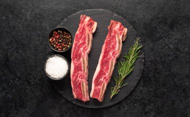 Çiğ domuz pirzolası, baharat ve siyah arka planda bitkiler.