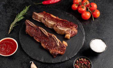 Baharatlı ızgara et ve siyah arka planda otlar.