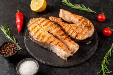 Sebzeli ızgara somon bifteği ve siyah taş arka planda baharatlar.