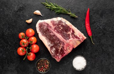 Baharatlı çiğ biftek ve siyah arka planda otlar.