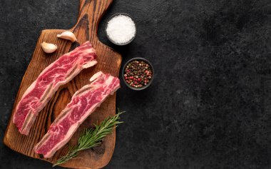 Çiğ domuz pirzolası, baharat ve siyah arka planda bitkiler.