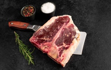 Baharatlı çiğ biftek ve siyah arka planda otlar.