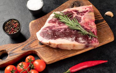 Baharatlı çiğ biftek ve siyah arka planda otlar.