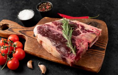 Baharatlı çiğ biftek ve siyah arka planda otlar.