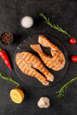 Sebzeli ızgara somon bifteği ve siyah taş arka planda baharatlar.