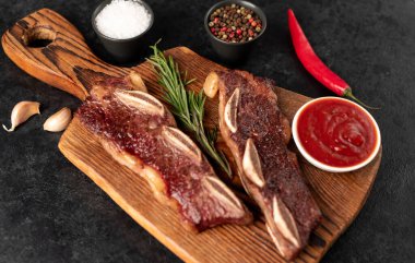 Baharatlı ızgara et ve siyah arka planda otlar.