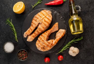 Sebzeli ızgara somon bifteği ve siyah taş arka planda baharatlar.