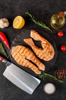 Sebzeli ızgara somon bifteği ve siyah taş arka planda baharatlar.