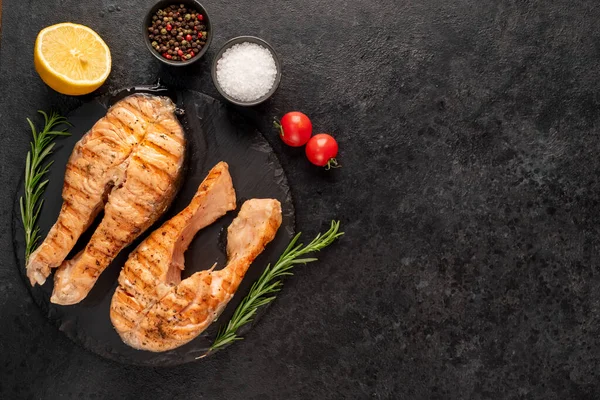 Sebzeli ızgara somon bifteği ve siyah taş arka planda baharatlar.