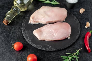 Baharatlı çiğ tavuk göğsü ve siyah arka planda otlar.