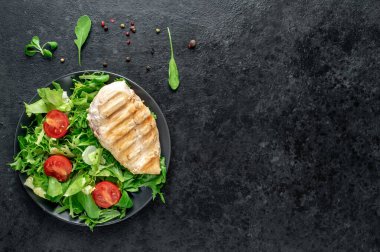 grilled chicken breast with vegetables  on a black plate. top view. 